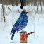 "Hand-painted Raven suncatcher, a stunning glass art piece hanging in a window. Perfect for bird lovers and nature-inspired home decor."